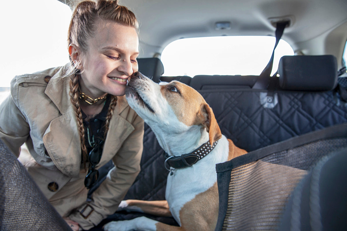 Dog laying on Meadowlark cargo liner protector smelling woman's face in the backseat of a vehicle